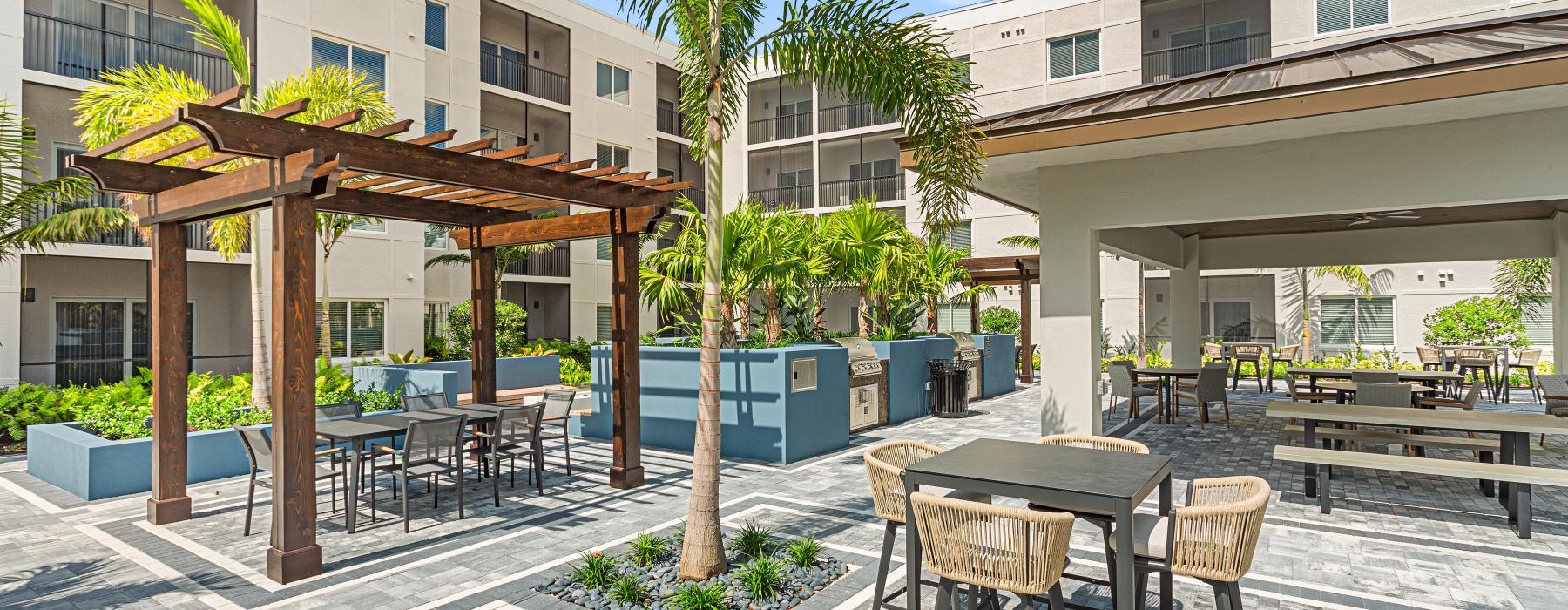 a patio with tables and chairs and trees in front of a building